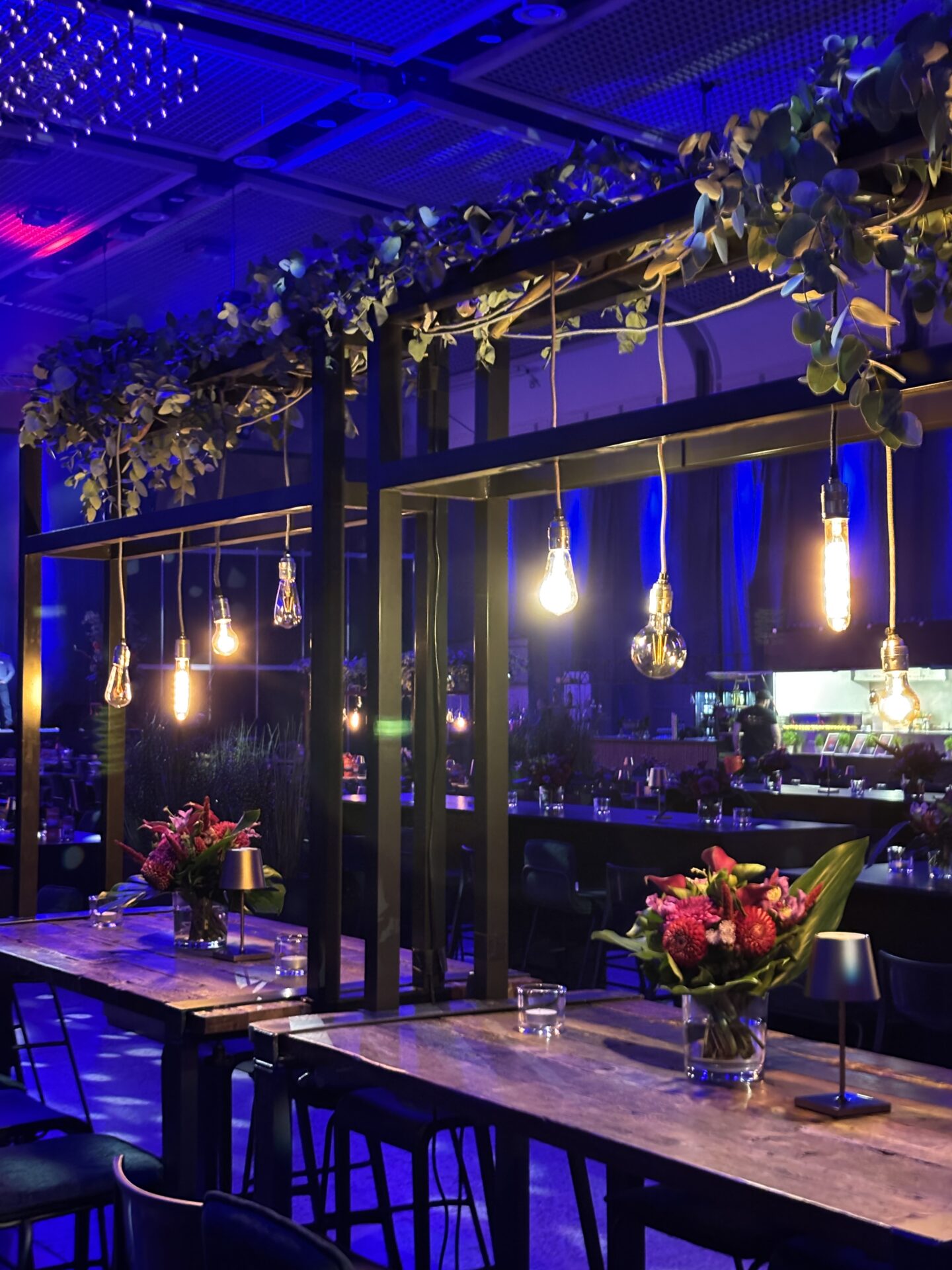 Stimmungsvolle Bar Lounge von Event Rent mit Edison Glühbirnen, Eukalyptus Girlande und blauer Ambientebeleuchtung.