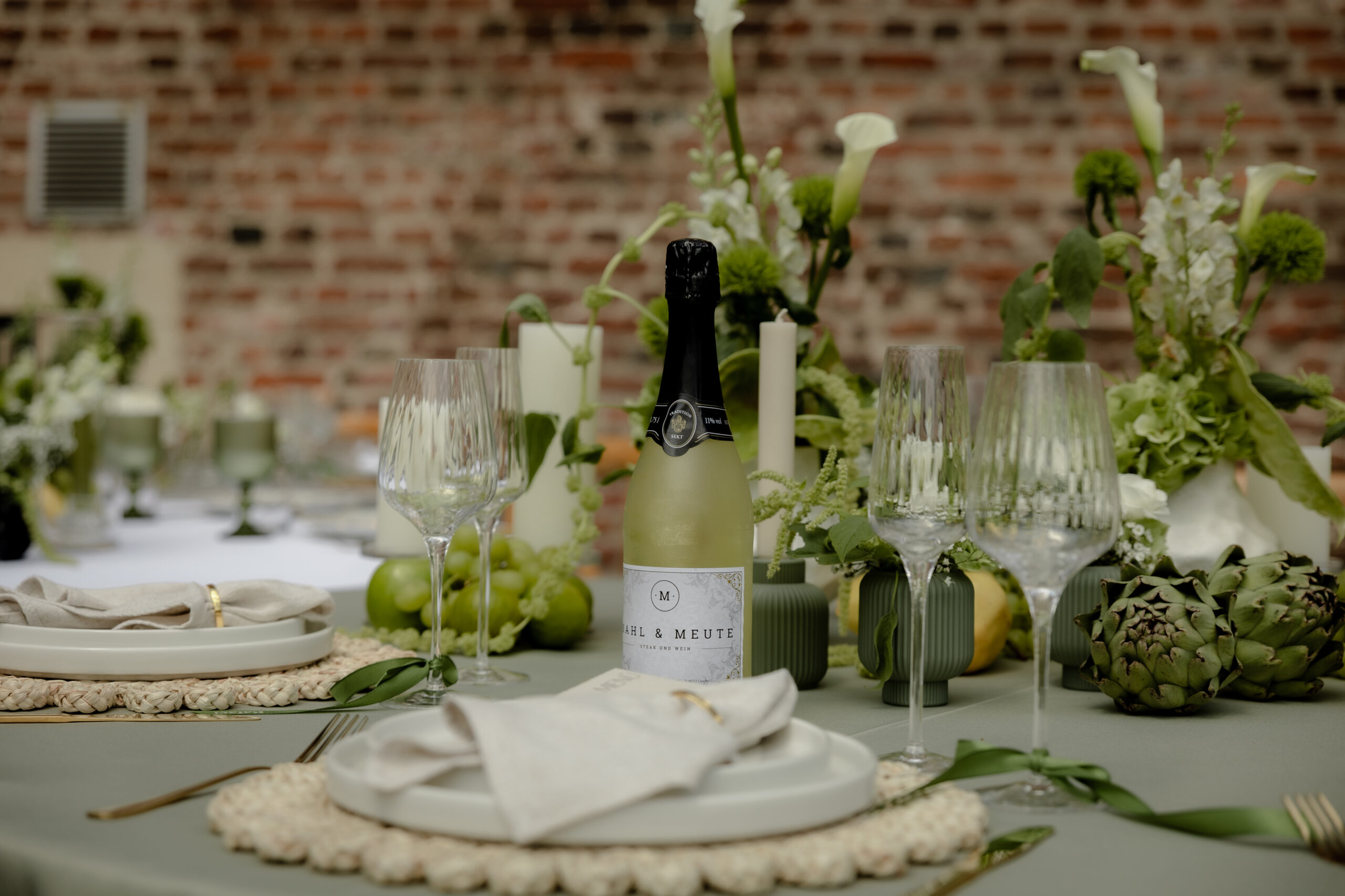 Festlich eingedeckter Tisch von Event Rent mit edlen Weingläsern, Sektflasche, Tellergedeck, Kerzen und grüner Blumendekoration für Hochzeiten.